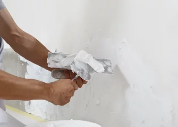 Hands man plasterer construction worker at work with trowel, plastering a wall, closeup